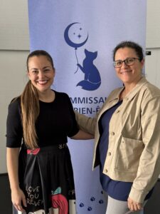 La présidente de la Coalition des parents en présence de la commissaire au bien-être devant un panneau déroulant présentant le logo du Bureau de la commissaire (renard bleu tenant un ballon-lune et les étoiles représentant les enfants